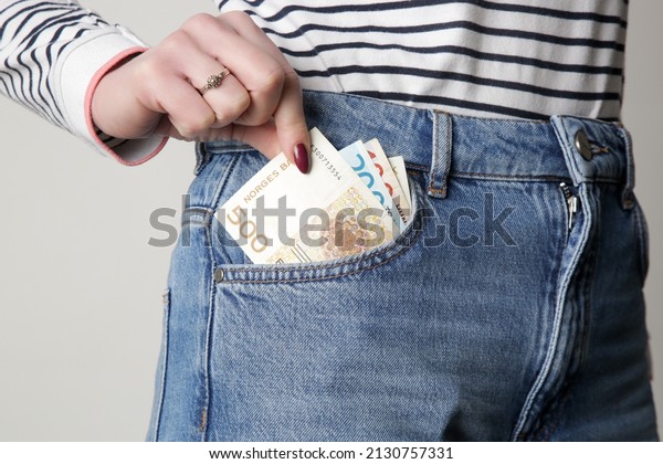 Woman holding Norwegian krone banknotes in pocket\
of her jeans