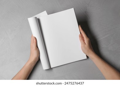 Woman holding notebook with blank pages at light grey table, top view. Mockup for design