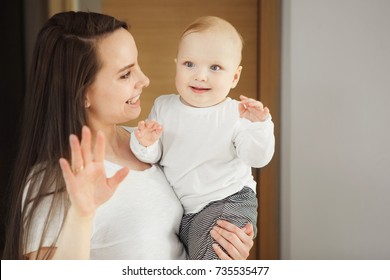 Woman Holding On Arms Her Adorable Baby Toddler, Proposing Him To Wave By Hand And Say Hello On Camera, Smiling Child With Mother