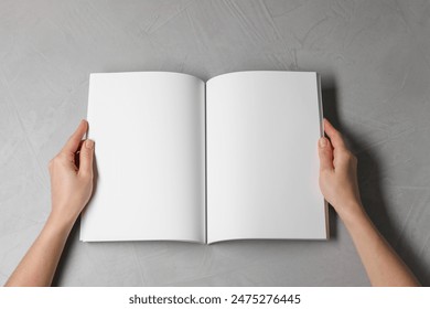 Woman holding open notebook with blank pages at light grey table, top view. Mockup for design