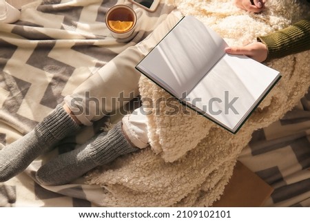 Woman holding opened book with blank pages and sitting on plaid in room