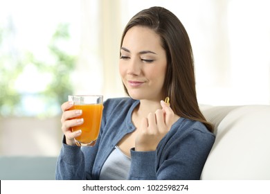 Woman Holding An Orange Juice And Vitamin Pill Sitting On A Couch In The Living Room At Home