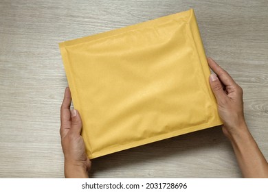 Woman holding padded envelope against wooden desk.Empty space for text