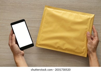Woman holding padded envelope and smartphone with white empty screen.Using internet for tracking and receive parcel.Top view