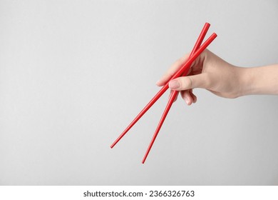 Woman holding pair of red chopsticks on light grey background, closeup. Space for text - Powered by Shutterstock