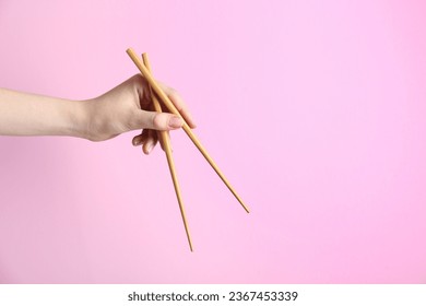 Woman holding pair of wooden chopsticks on pink background, closeup. Space for text - Powered by Shutterstock