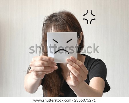A woman holding a paper with an angry face illustration in her hands in front of her face
