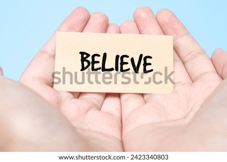 Woman holding paper in hand spelling words Believe with blue background. Torn piece of paper with the word 