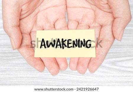 Woman holding paper  in hands spelling words Awakening with blue background. Torn piece of paper with the word 