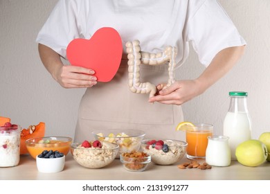 Woman Holding Paper Heart And Large Intestine Model Near Table With Food, Closeup. Balanced Nutrition For Healthy Digestive System