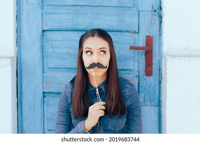 Woman Holding a Paper Mustache Looking Sideways. Young person showing bubbly personality holding party accessory
