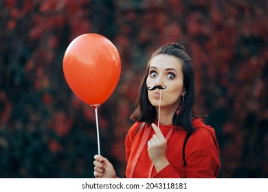 Woman Holding Paper Mustache Party Accessory and Red balloon. Quirky girl holding a party accessory celebrating anniversary or festive carnival event
				
