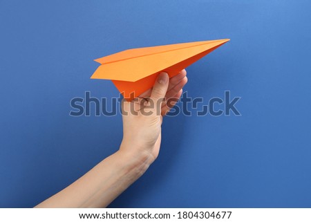 Woman holding paper plane on blue background, closeup