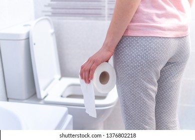 Woman holding a paper roll and suffering from diarrhea, constipation and cystitis at toilet. Treatment stomach pain and health care
