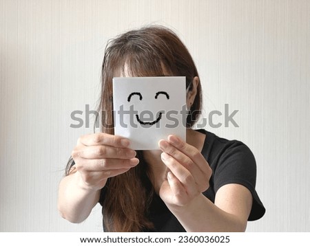A woman holding a paper with a smiling face in both hands in front of her face