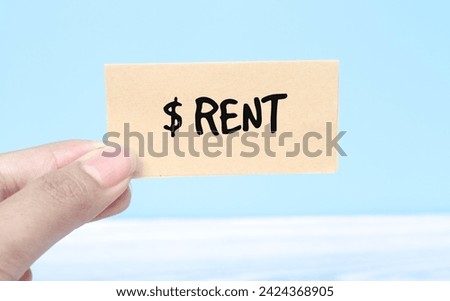 Woman holding paper spelling words RENT with US dollar bills on blue background. Torn piece of paper with the word 