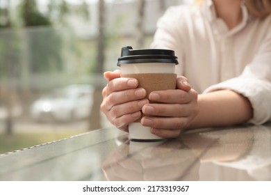 Woman holding paper takeaway cup at glass table outdoors, closeup. Coffee to go