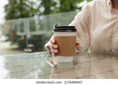 Woman holding paper takeaway cup at glass table outdoors, closeup. Coffee to go