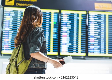 ํํYoung woman holding a passport is standing looking at an airport information board in the airport. To check the flight time of her own. Traveling concept - Shutterstock ID 1162823041