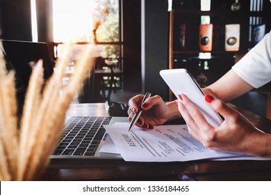 woman holding pen over resume application with smart phone and using computer laptop to job search on online internet. applying for a job concept.