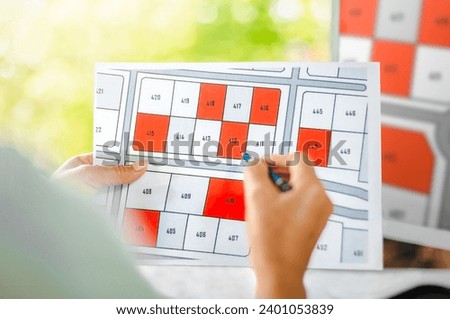 Woman holding a pencil pointing to cadastral map to decide to buy land. real estate concept with vacant land for building construction and housing subdivision for sale, rent, buy, investment.