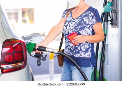 Woman holding petrol gasoline fuel pump to refuel her silver car at the service station, holding wallet to pay