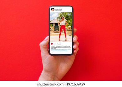 Woman holding phone in hand with photo of fashion model in red pants on red background - Shutterstock ID 1971689429