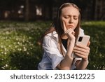 Woman holding a phone while holding her hand on chin. Expressive student thinking outside in campus - Woman in doubt with smartphone in her palm, think about reading information, search solution.