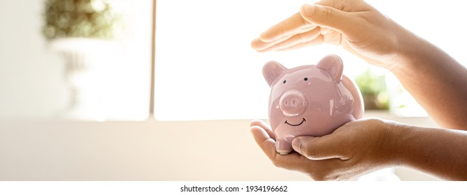 A Woman Holding A Piggy Bank In The Shape Of A Pink Pig, She Is Organizing Money To Divide It Into Savings And Buy Funds To Make It Grow. Personal Finance Concept.