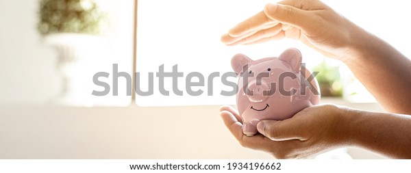 A woman holding a piggy
bank in the shape of a pink pig, she is organizing money to divide
it into savings and buy funds to make it grow. Personal finance
concept.