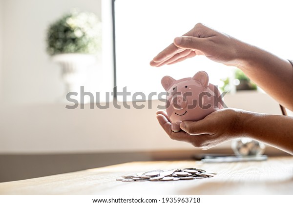 A woman holding a piggy\
bank in the shape of a pink pig, she is organizing money to divide\
it into savings and buy funds to make it grow. Personal finance\
concept.