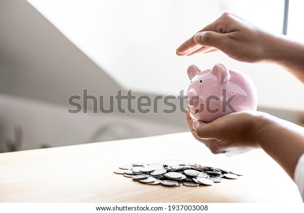A woman holding a piggy\
bank in the shape of a pink pig, she is organizing money to divide\
it into savings and buy funds to make it grow. Personal finance\
concept.
