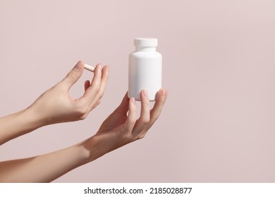 Mujer sosteniendo una píldora y un tubo blanco de plástico en el fondo rosado. Envase para píldora, cápsula o suplemento. Mochila de marca de productos módicos. Foto de alta calidad