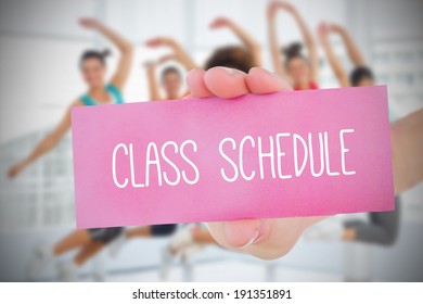 Woman Holding Pink Card Saying Class Schedule Against Fitness Class In Gym