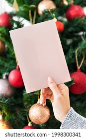 Woman holding a pink Christmas card in front of a Christmas tree mockup
