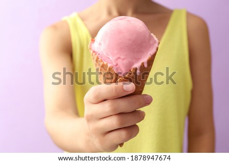 Woman holding pink ice cream in wafer cone on violet background, closeup