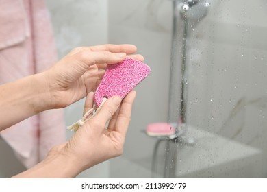 Woman Holding Pink Pumice Stone Near Shower Stall In Bathroom, Closeup. Space For Text