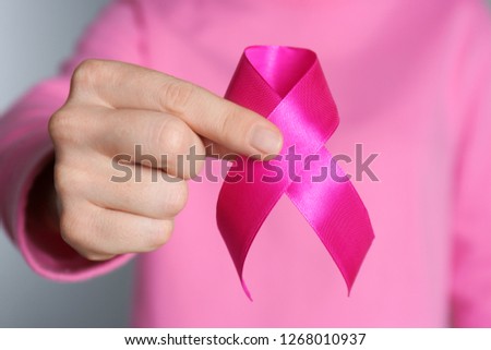 Woman holding pink ribbon on grey background, closeup. Breast cancer awareness