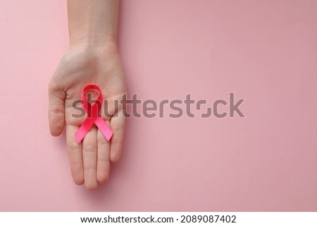 Woman holding pink ribbon on color background, top view with space for text. Breast cancer awareness concept