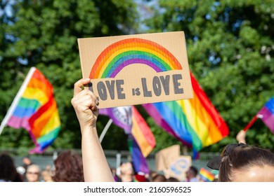 Woman holding placard sign Love is Love with rainbow symbol of LGBT community. Crowd with flags in background. Pride Parade, equality march to support and celebrate LGBT+, LGBTQ Gay lesbian equality.