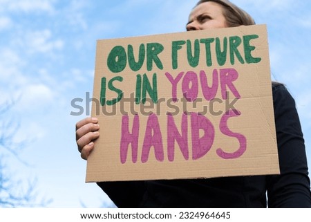 Woman holding placard sign with text Our Future Is In Your Hands. Female protestor with cardboard banner at protest rally demonstration. Strike against climate change and global warming.