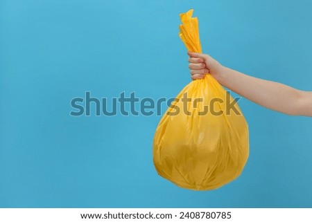 Woman holding plastic bag full of garbage on light blue background, closeup. Space for text