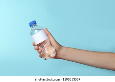 Woman holding plastic bottle of pure water with blank tag on color background