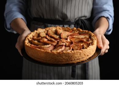 Woman holding plate with delicious apple pie on black background, closeup