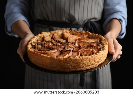 Woman holding plate with delicious apple pie on black background, closeup