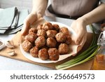 Woman holding plate with delicious meatballs at light textured table, closeup