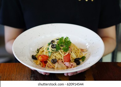 Woman Holding Plate Of Spicy Spaghetti Bacon - Spaghetti With Bacon, Basil, Garlic, Tomato, Black Olive On Top Parmesan Cheese And Parsley.