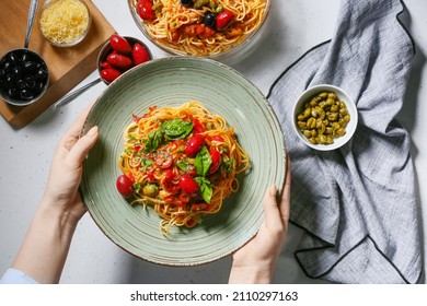 Woman holding plate with tasty Pasta Puttanesca at table