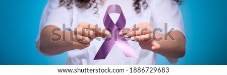 Woman holding purple ribbon symbol of breast cancer awareness pink ribbon. Isolated blue background