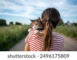 Woman holding quiet tabby cat in arms. Pet looking around, exploring territory with interest, curiosity, feeling cozy, comfortable in hands of female owner. Girl strolling with kitty together.